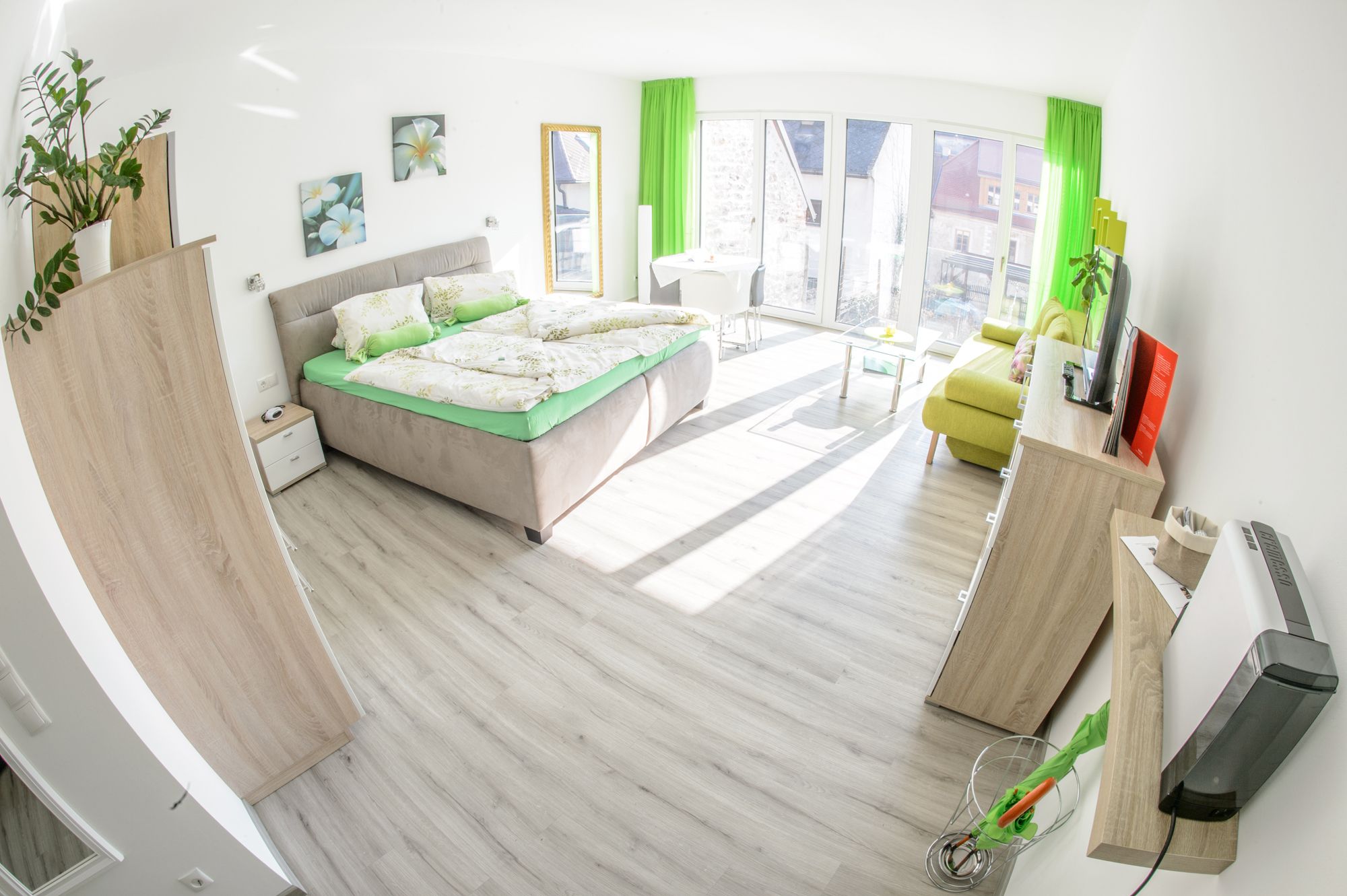 Svetlá izba pre hostí s manželskou posteľou, pohovkou, TV a veľkými oknami.