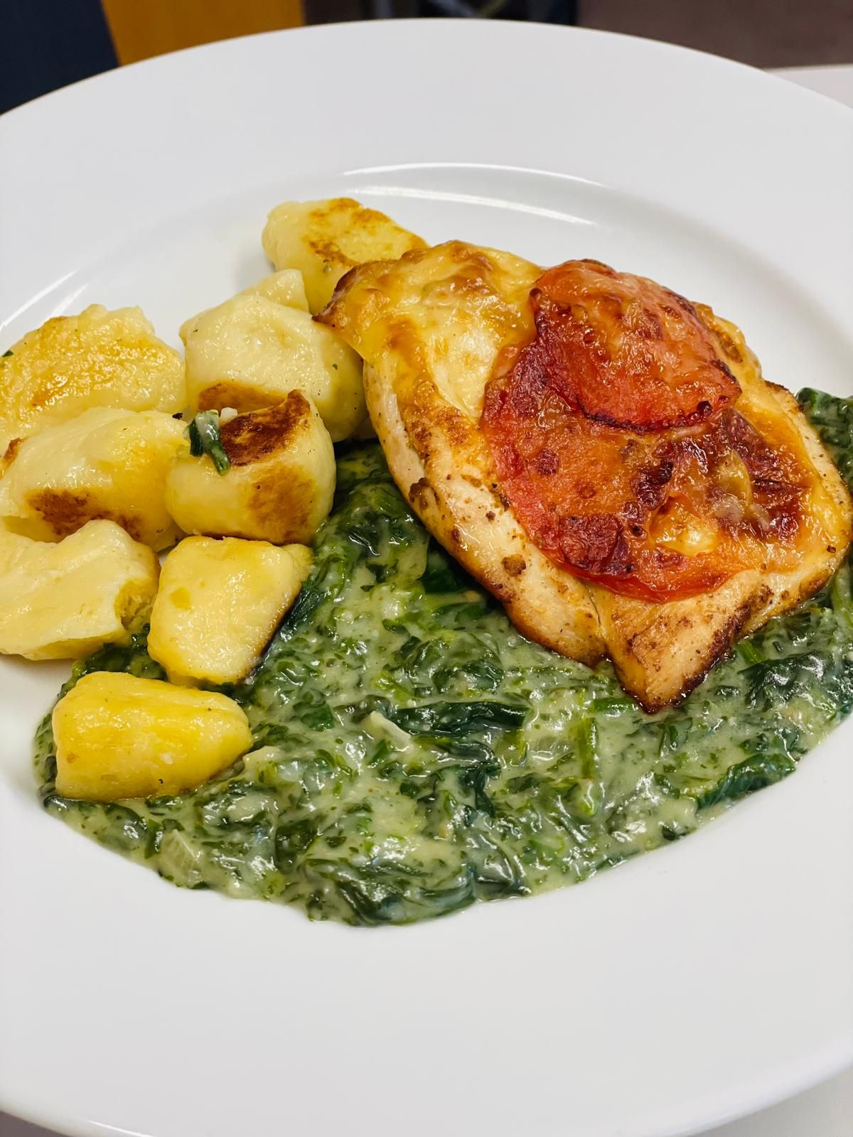 Tanier s gnocchi, krémovým špenátom a zapečeným kuracím mäsom s plátkom paradajky.