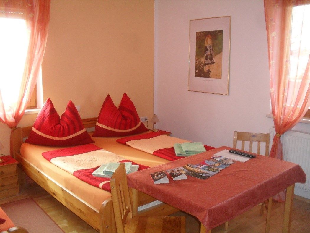Útulná spálňa s manželskou posteľou, červenými vankúšmi a stolíkom s brožúrami.