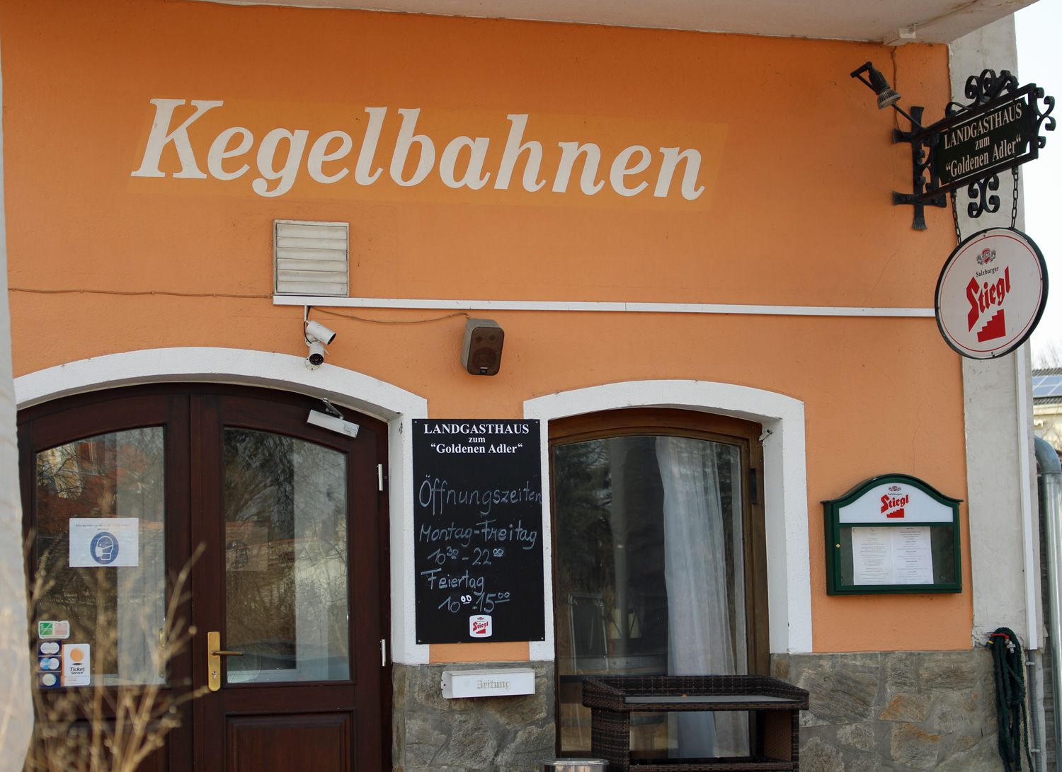Vchod do vidieckeho hostinca s nápisom "Kegelbahnen" a nápisom Stiegl beer.