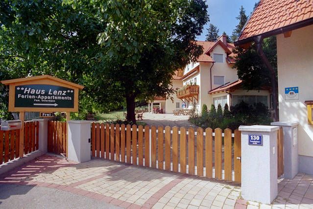 Vchod do domu Haus Lenz s dreveným plotom a nápisom, obklopený stromami.