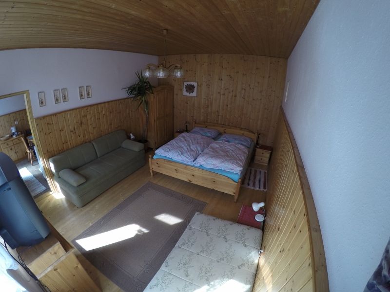 Útulná spálňa s drevenými stenami, manželskou posteľou, pohovkou a kobercom na drevenej podlahe.