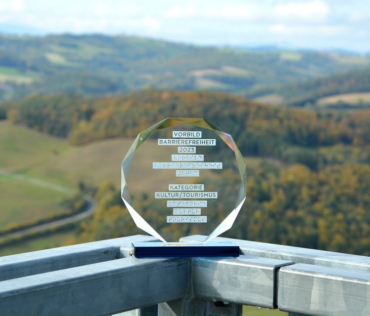 Ocenenia za prístupnosť 2023 stojí na zábradlí s krajinou v pozadí. Vyhliadková plošina je prístupná pomocou výťahu.