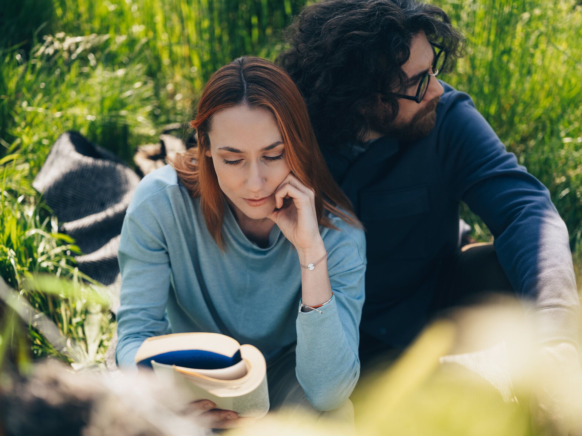 Inmitten der sanften Hügel und üppigen Wiesen genießen zwei Freunde eine entspannte Lesepause. Die warmen Sonnenstrahlen durchdringen das grüne Blätterdach und schaffen eine harmonische Atmosphäre, die zum Verweilen einlädt.