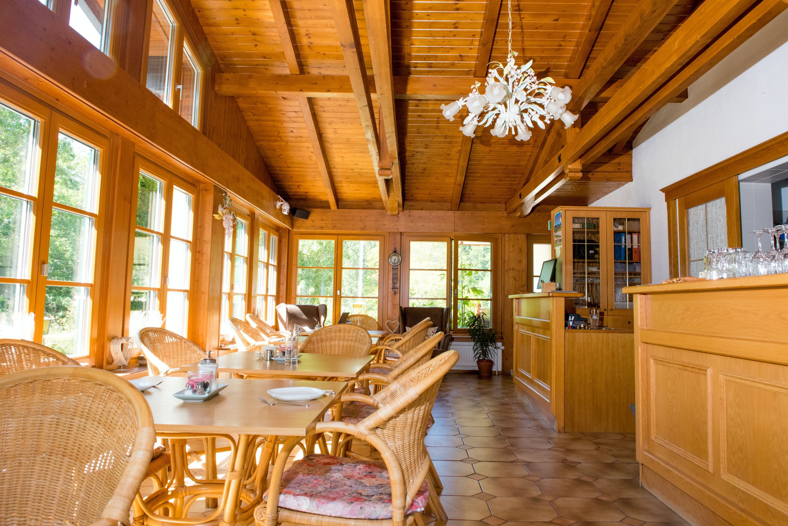 Svetlá raňajková miestnosť s dreveným nábytkom, veľkými oknami a lustrom.