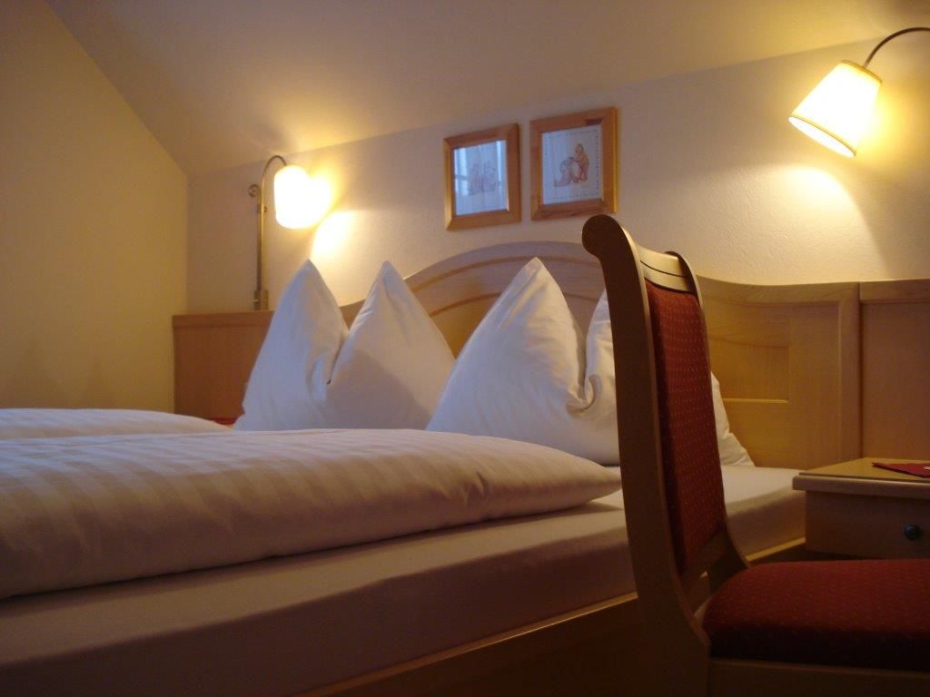 Útulná izba pre hostí s manželskou posteľou, dvoma nočnými lampami a stoličkou.