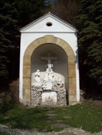 Malá kaplnka s krížom a náboženskými postavami vo výklenku.
