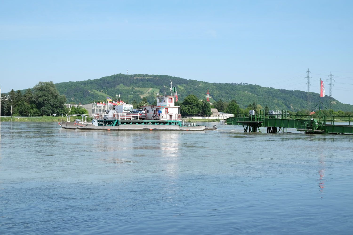 Valiaci sa trajekt na Dunaji v Korneuburgu-Klosterneuburgu so zelenou krajinou v pozadí.