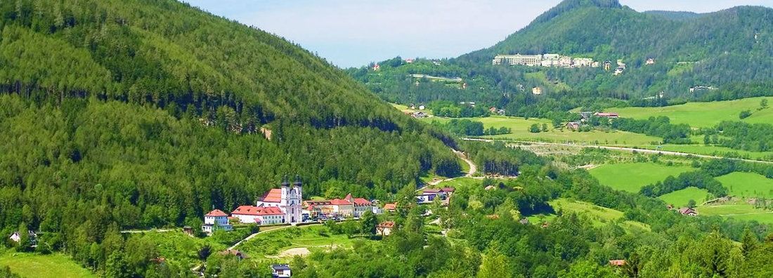 Krajina s kostolom a zelenými kopcami v popredí.