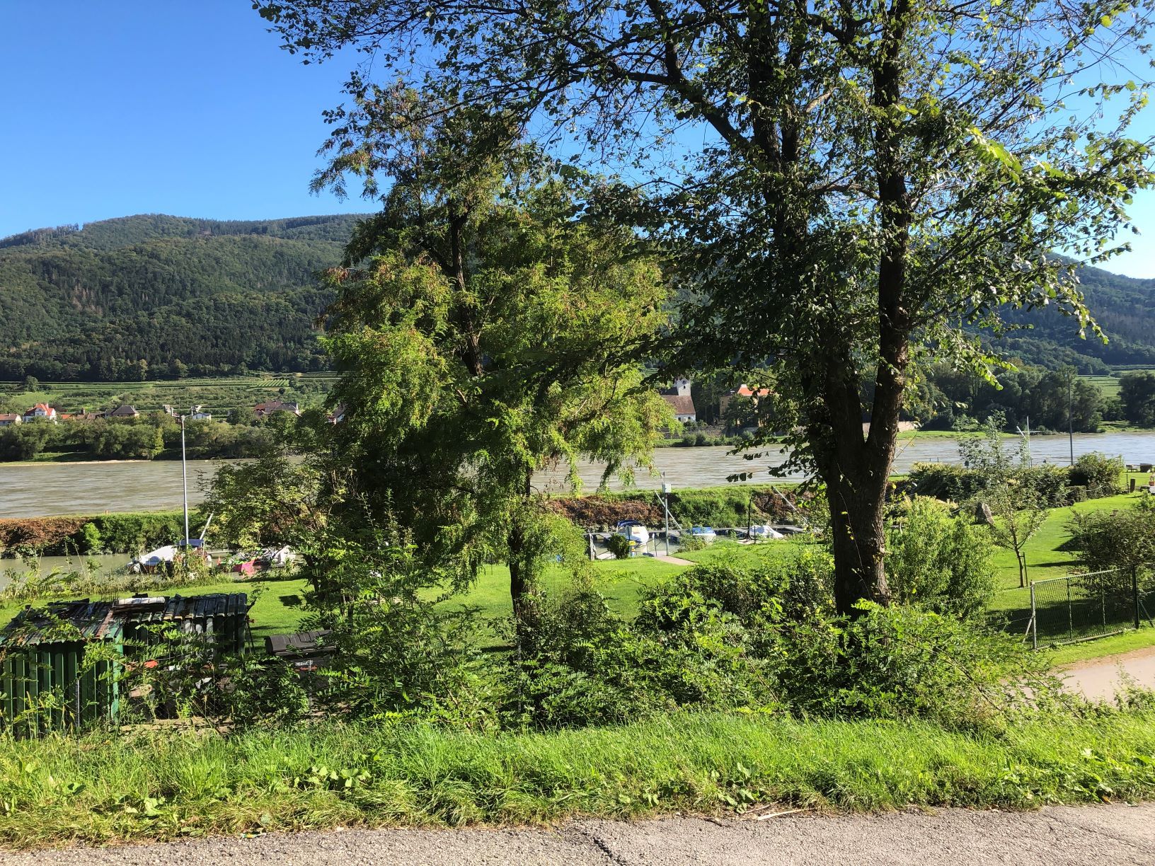 Krajina s Dunajom, stromami a loďami v pozadí.