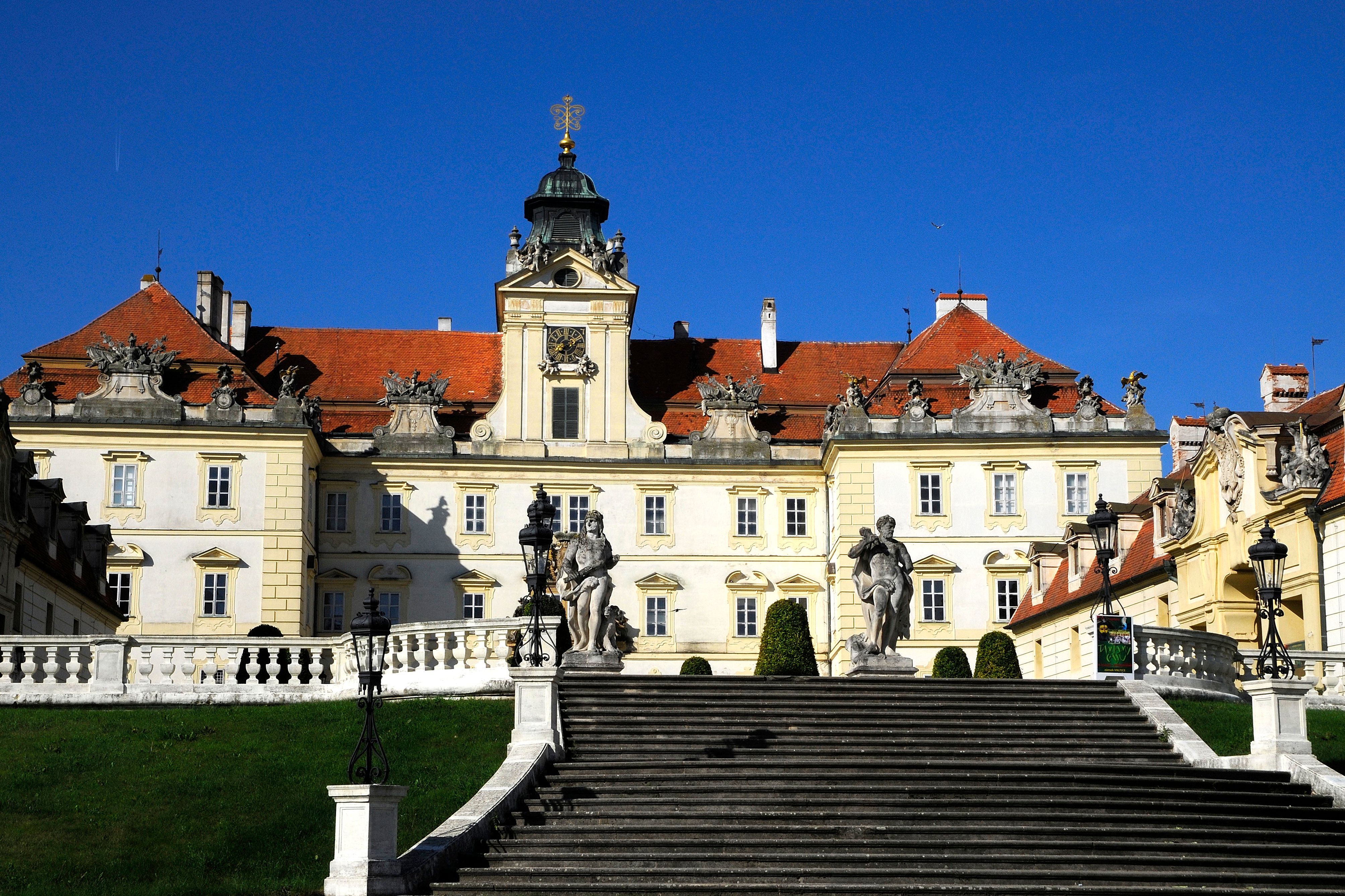 Pohľad na Valtický hrad spredu so schodiskom a sochami v popredí.