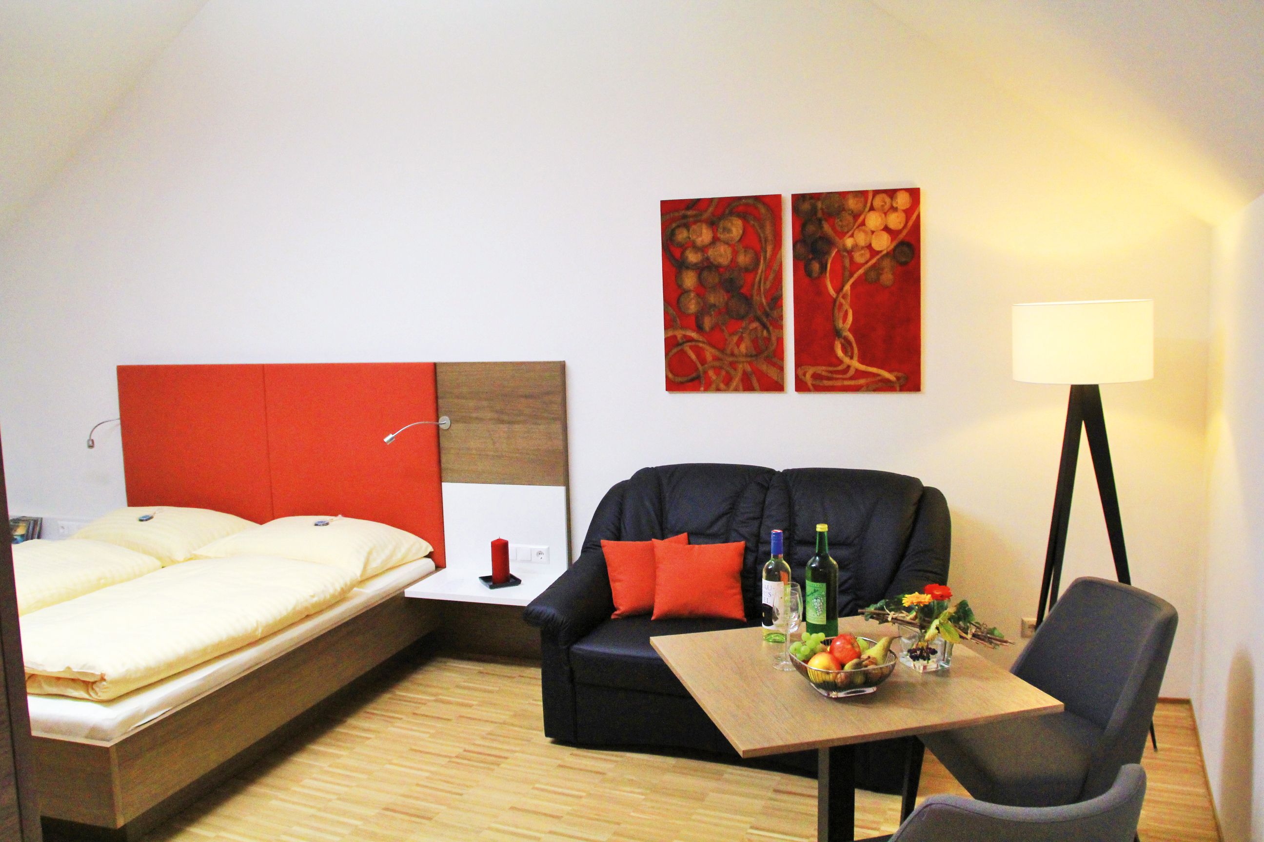 Útulná izba s manželskou posteľou, pohovkou, stolom a stojacou lampou.