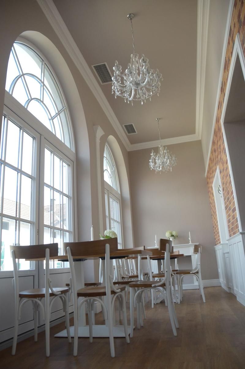 Elegantná izba s vysokými oknami, lustrami a dreveným nábytkom.