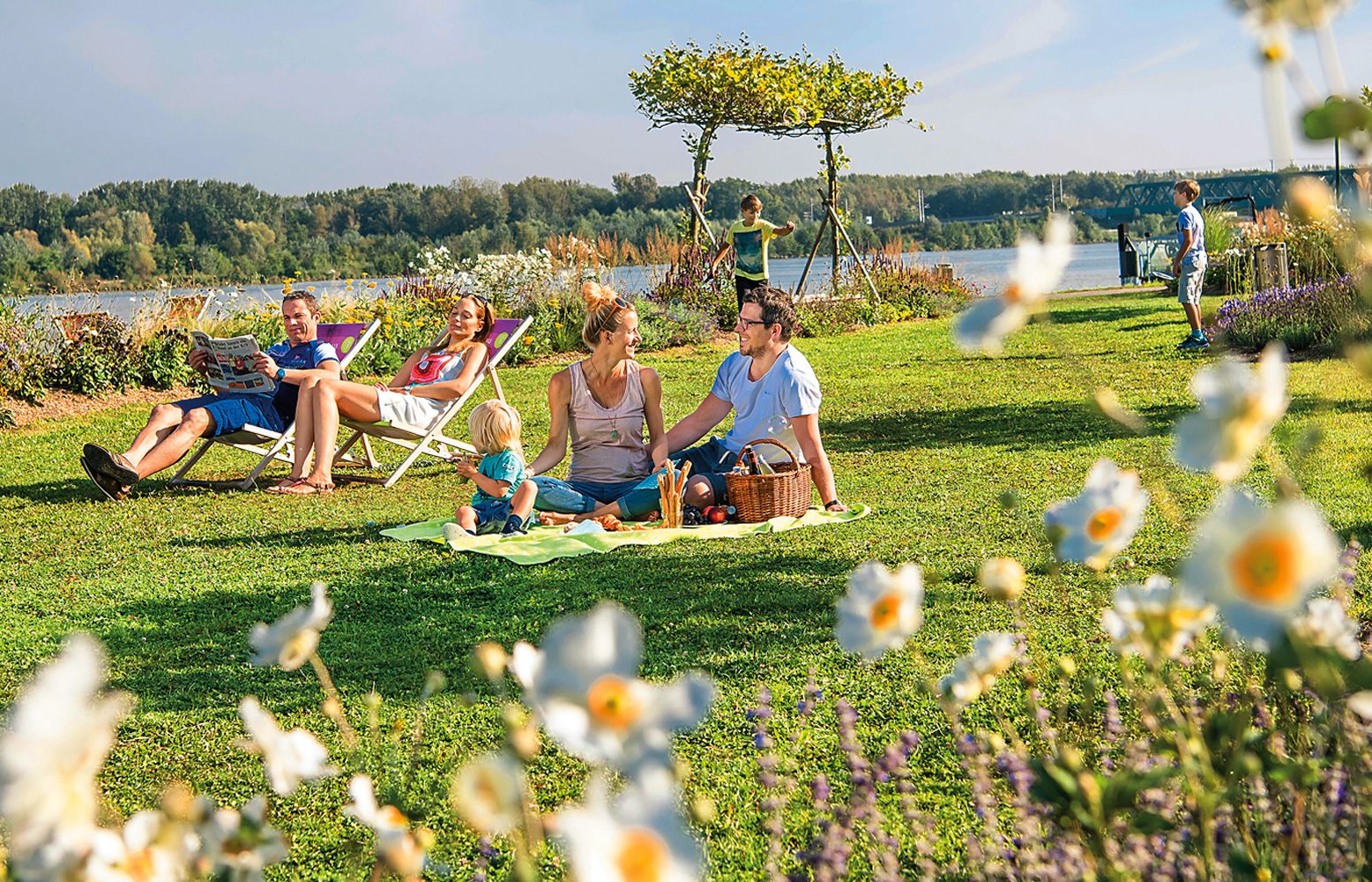 Rodinný piknik na vidieku s kvetmi v popredí a riekou v pozadí.