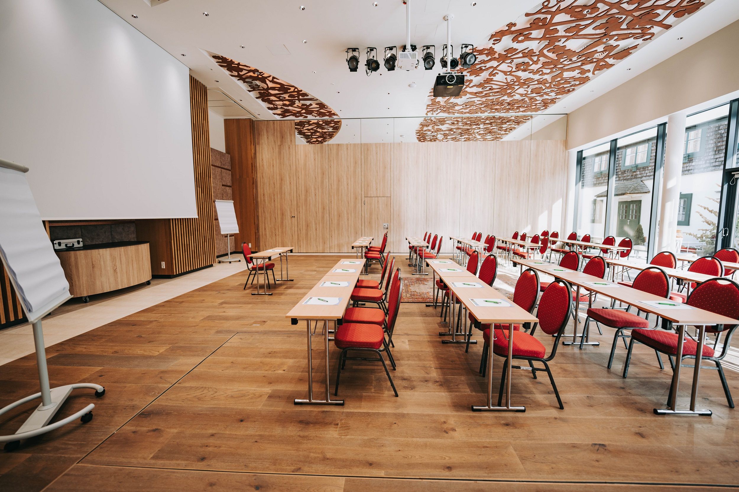Pohľad do interiéru modernej konferenčnej miestnosti s červenými stoličkami a drevenou podlahou.
