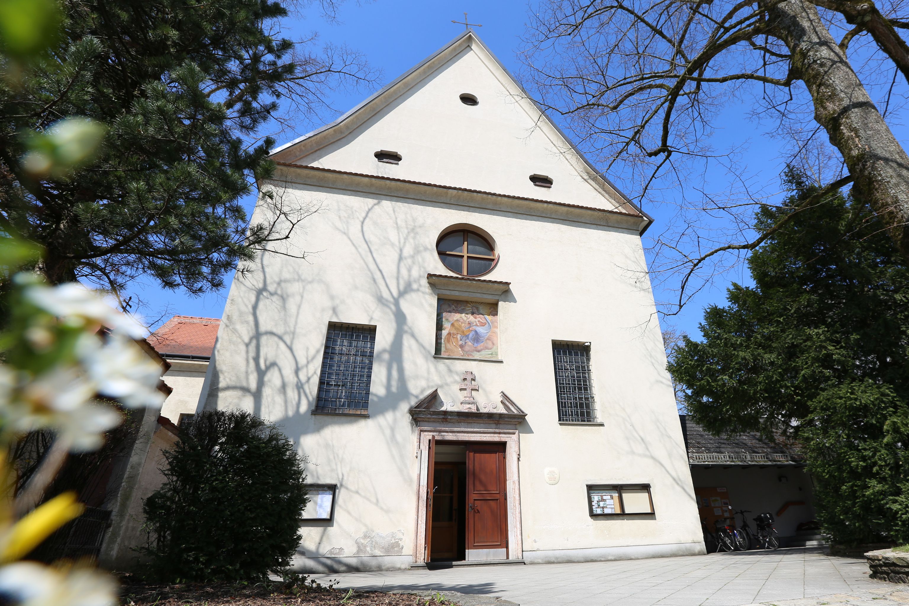 Fasáda kapucínskeho kostola s vchodom a oknami, obklopená stromami.