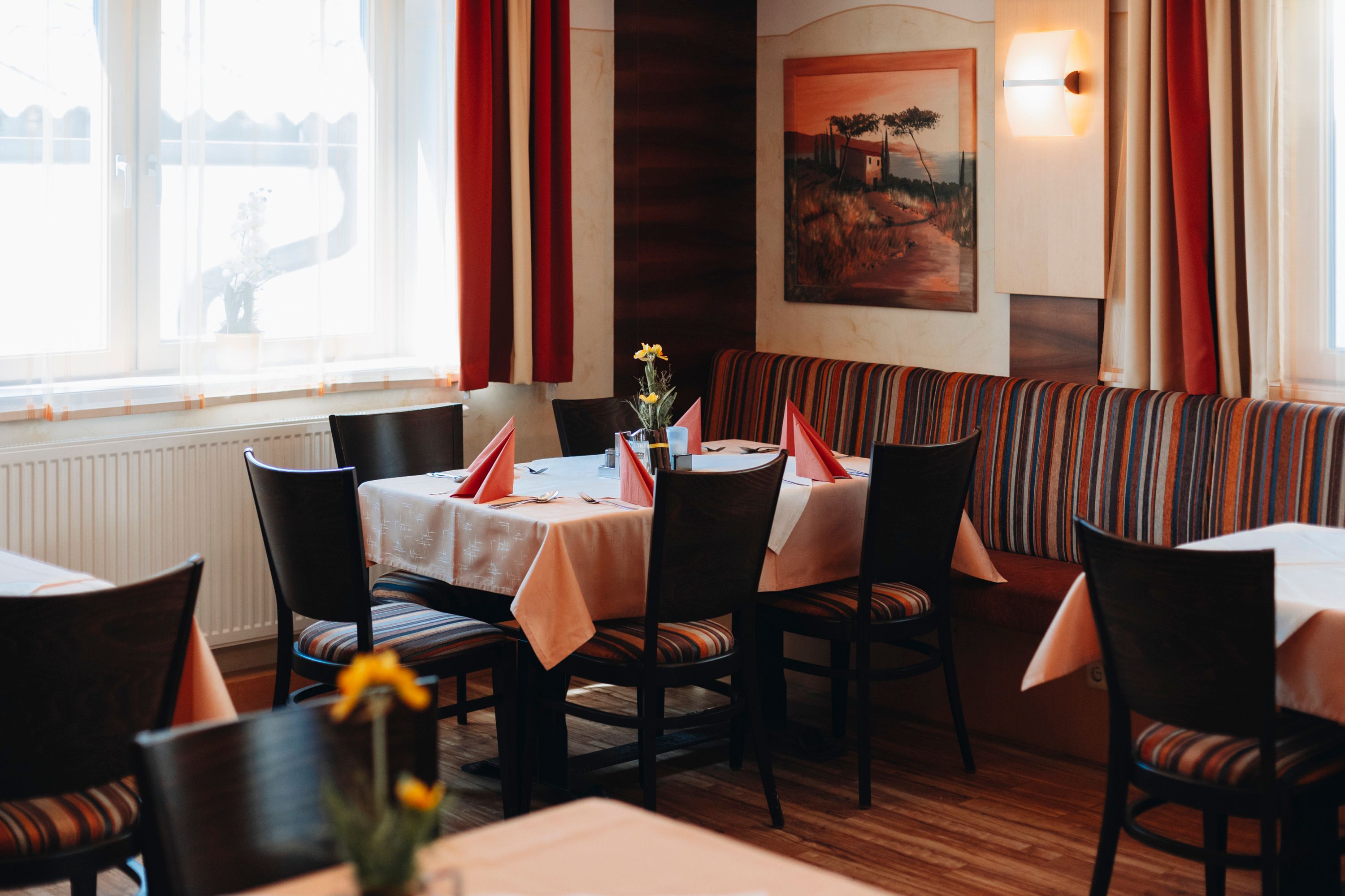 Útulná reštaurácia s prestretým stolom, červenými obrúskami a kvetmi.