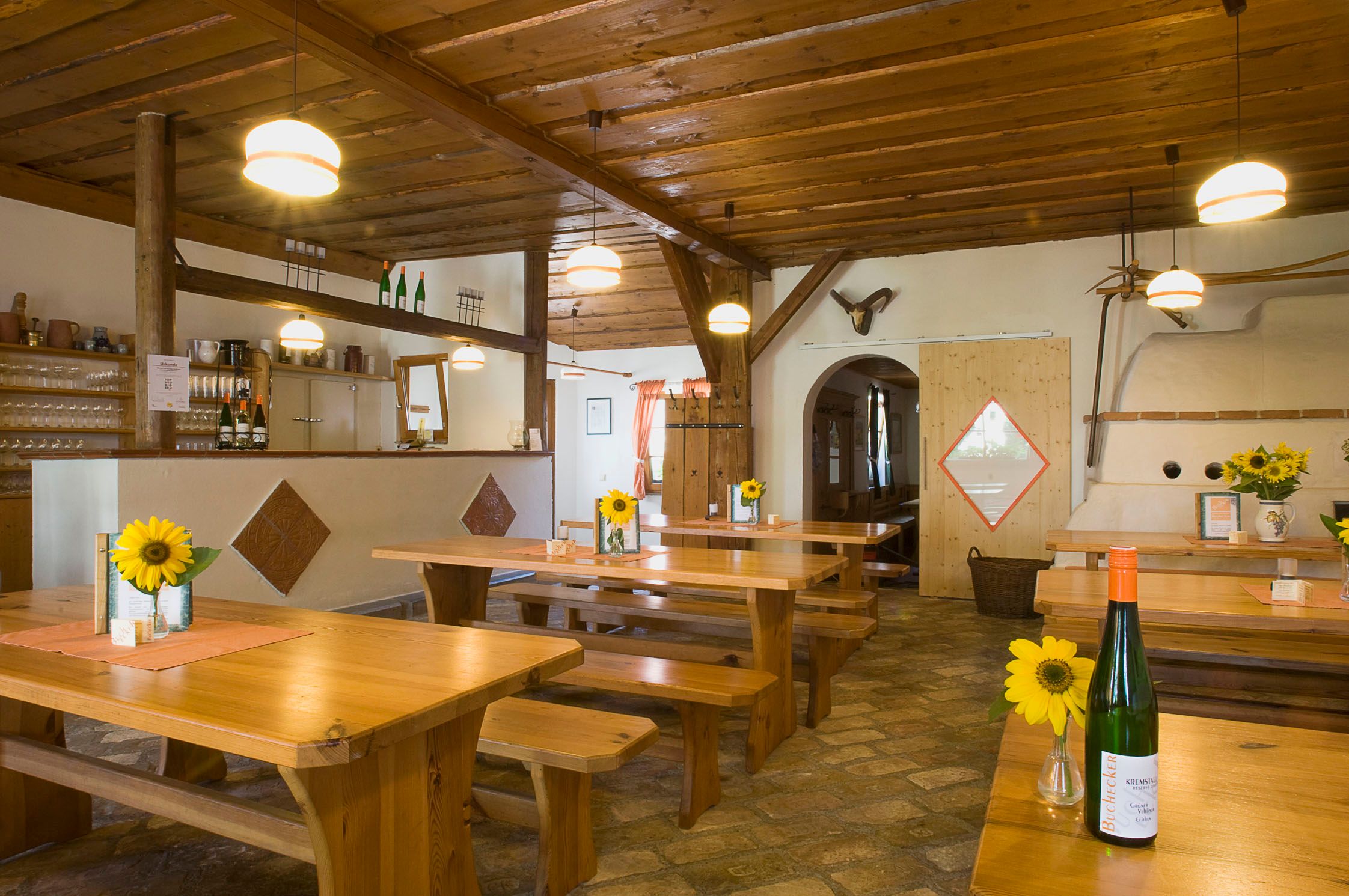 Pohľad do interiéru tradičnej vinárne s drevenými stolmi, slnečnicami a fľašami vína.