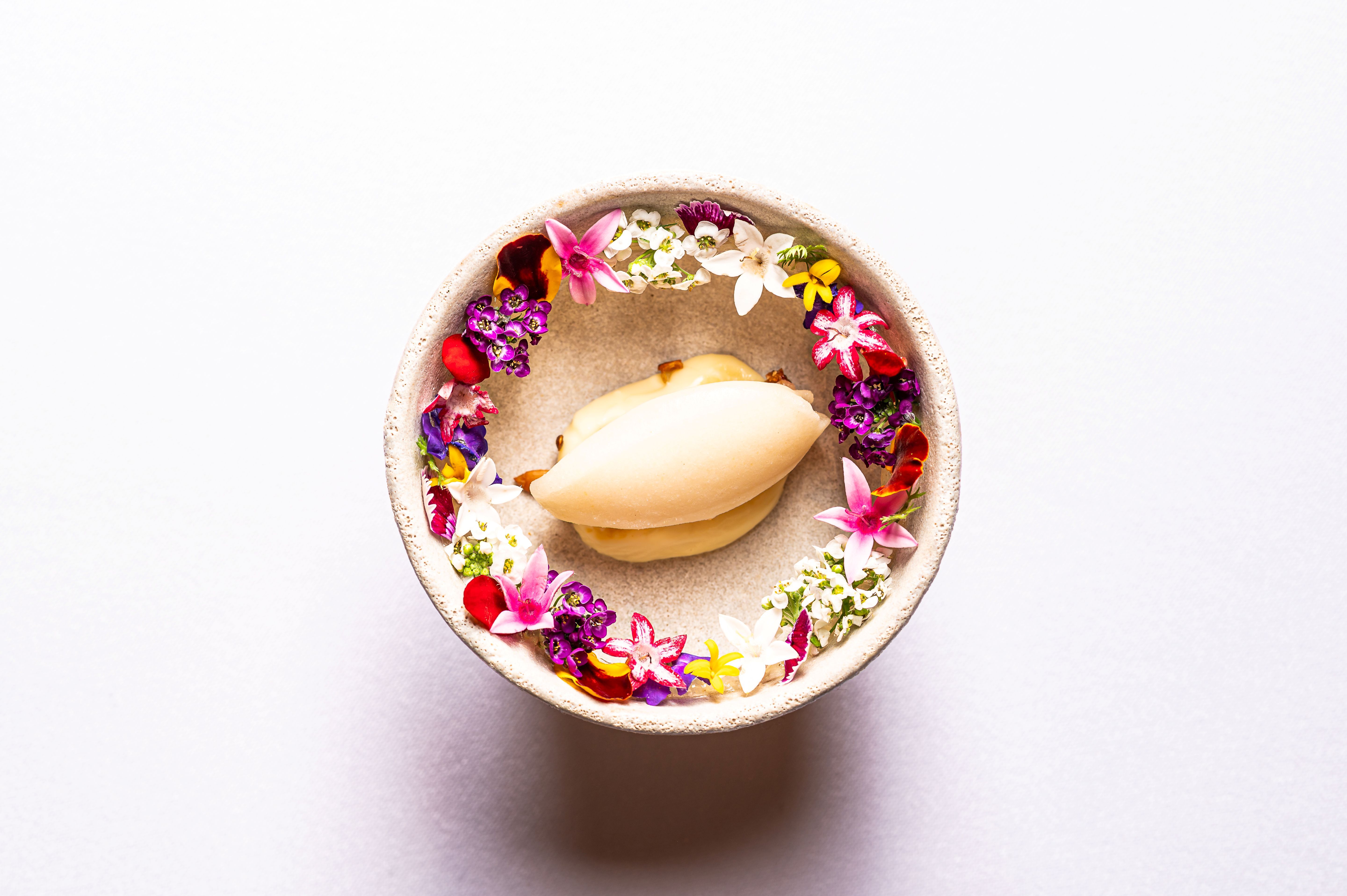 Dezert v miske obklopený farebnými jedlými kvetmi.