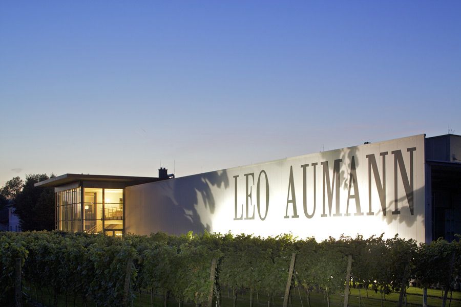 Budova s nápisom "Leo Aumann" za súmraku, obklopená viničom.