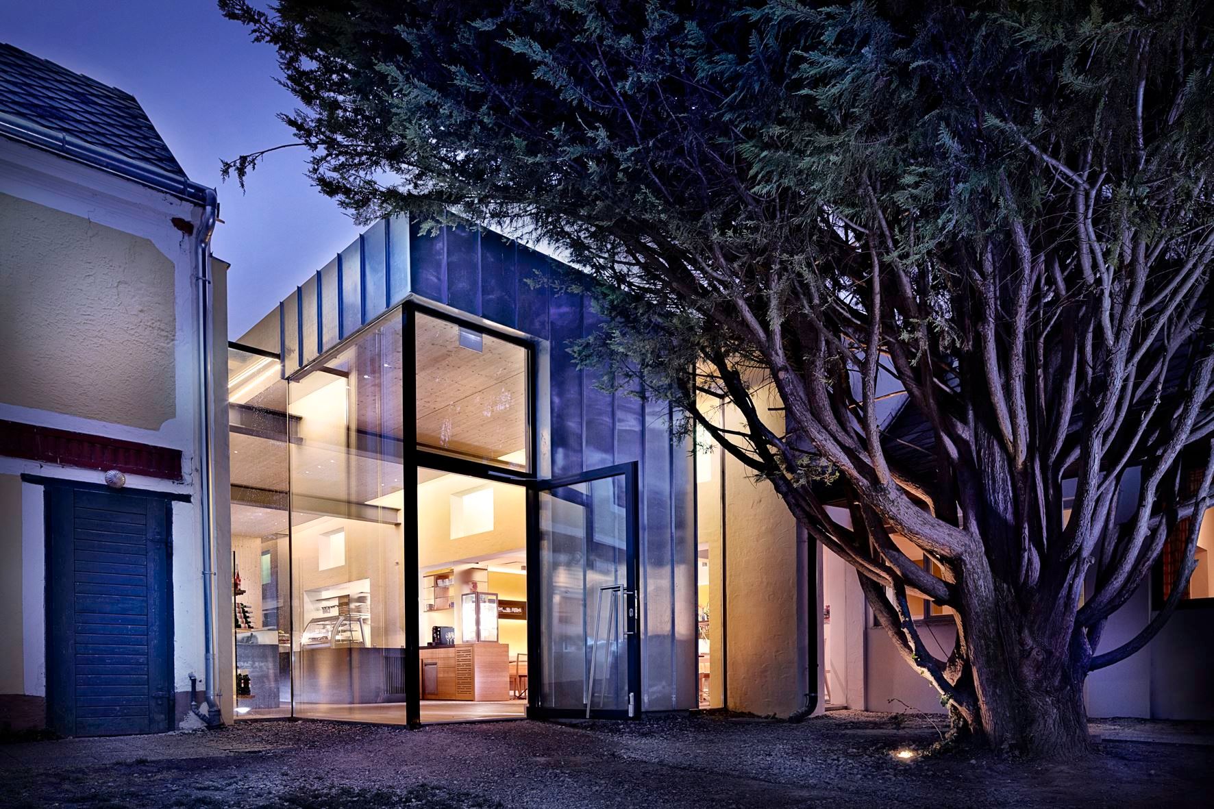 Moderná sklenená fasáda budovy v noci, obklopená stromami.