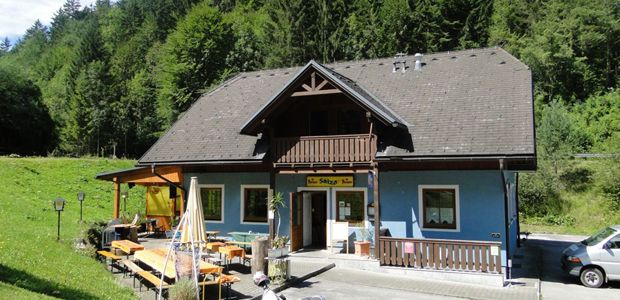 Modrá budova s dreveným balkónom a terasou, obklopená stromami.