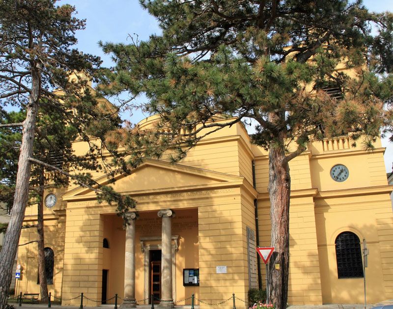 Vonkajší pohľad na faru Hinterbrühl so žltou fasádou a hodinami.