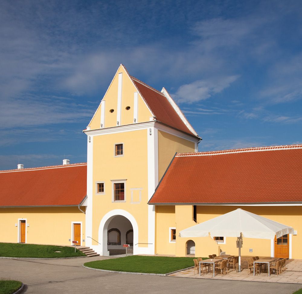 Žltá budova s červenou strechou a oblúkom, modrá obloha v pozadí.