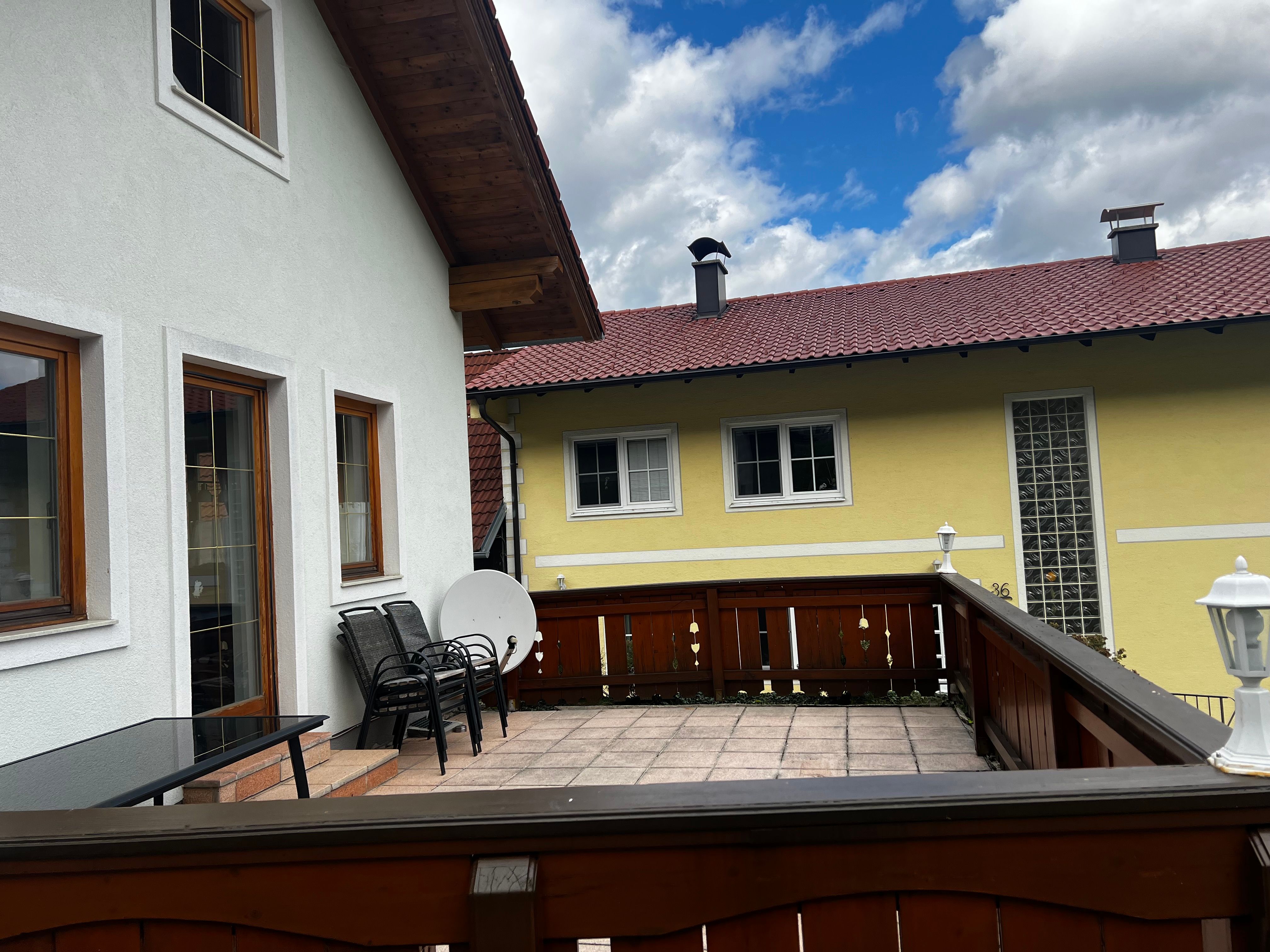 Terasa bytu s dreveným nábytkom a výhľadom na žltý susedný dom s červenou strechou.