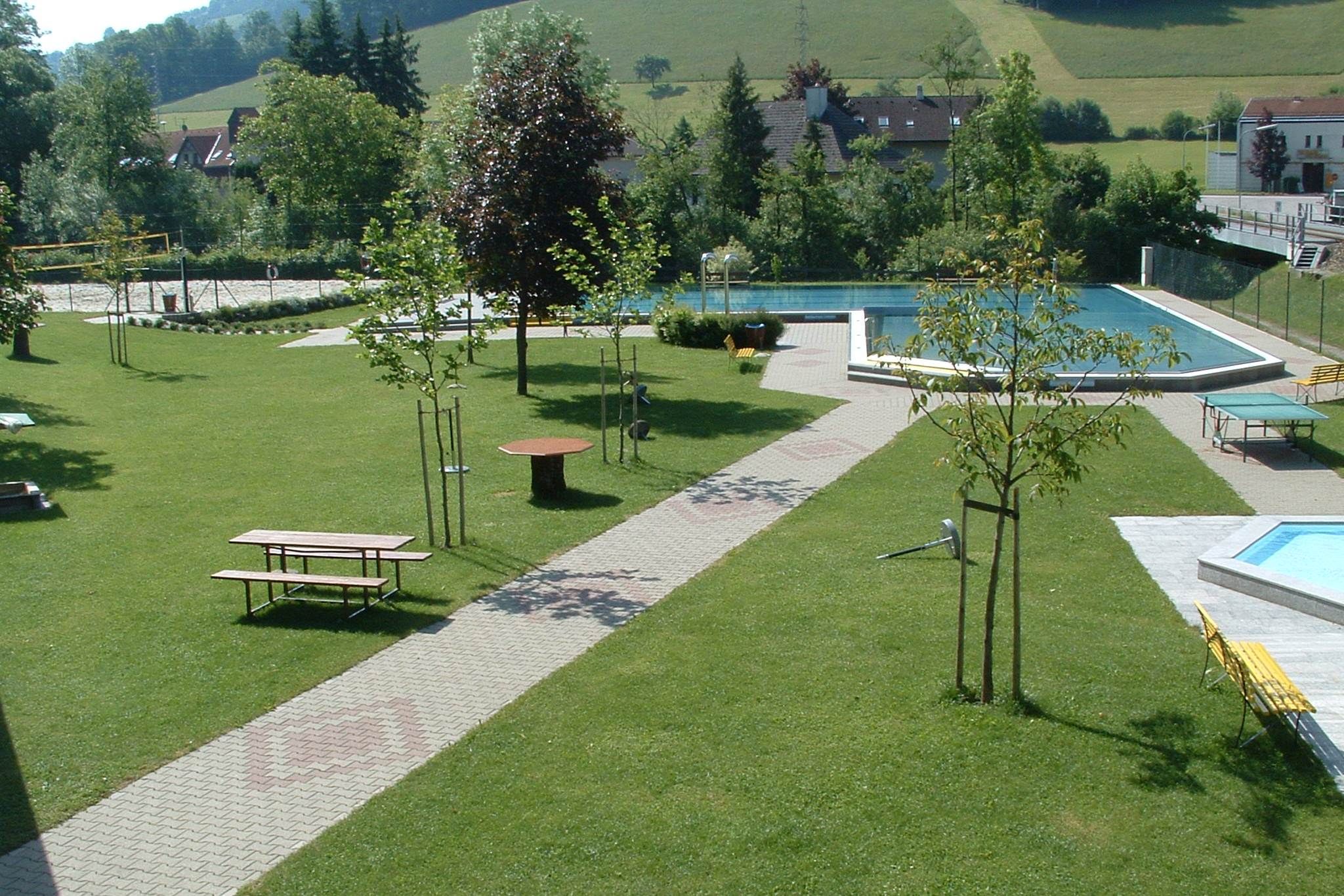 Zelený park s bazénom a lavičkami.