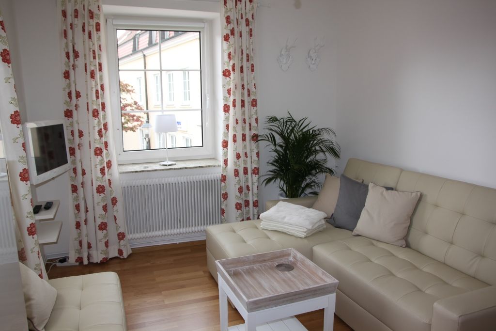 Svetlá obývacia izba s béžovou pohovkou, vankúšmi, konferenčným stolíkom a oknom so závesmi.