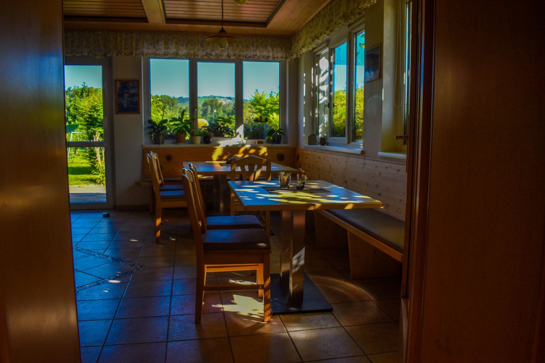 Útulná raňajková miestnosť s dreveným nábytkom a veľkými oknami prepúšťajúcimi slnečné svetlo.