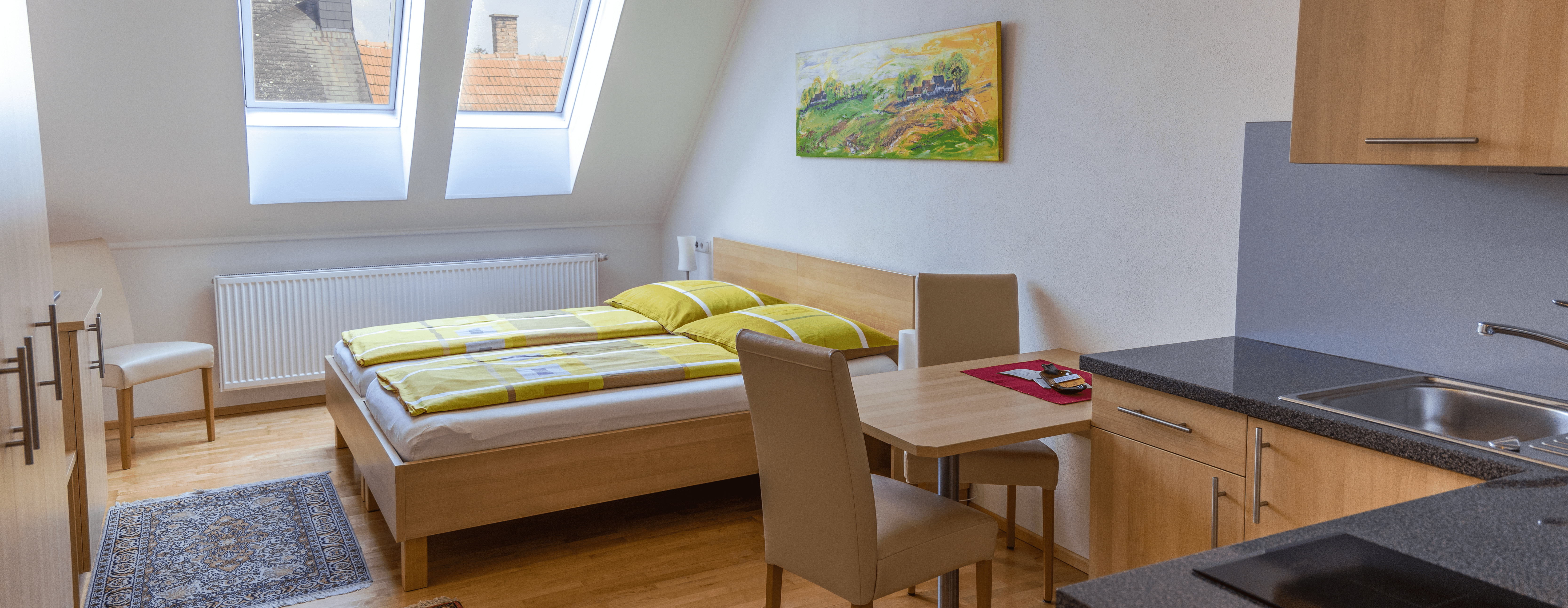 Dvojlôžková izba s kuchynským kútom, posteľou, stolom a stoličkami.