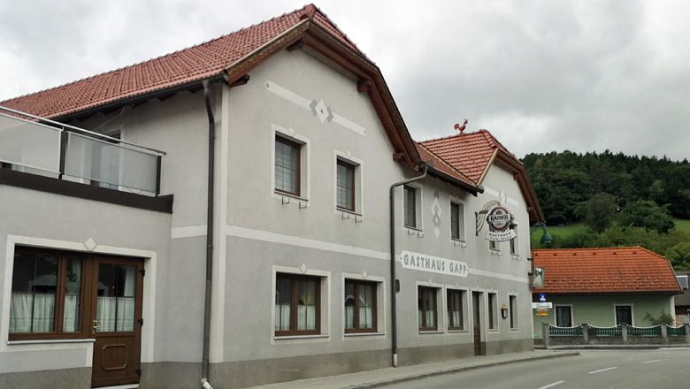 Gasthaus Gapp vo Weinburgu so sivou fasádou a červenou strechou.