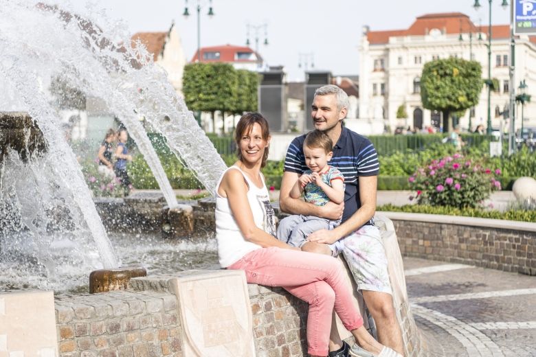 Usmiata rodina sedí pri fontáne na hlavnom námestí v Tullne.