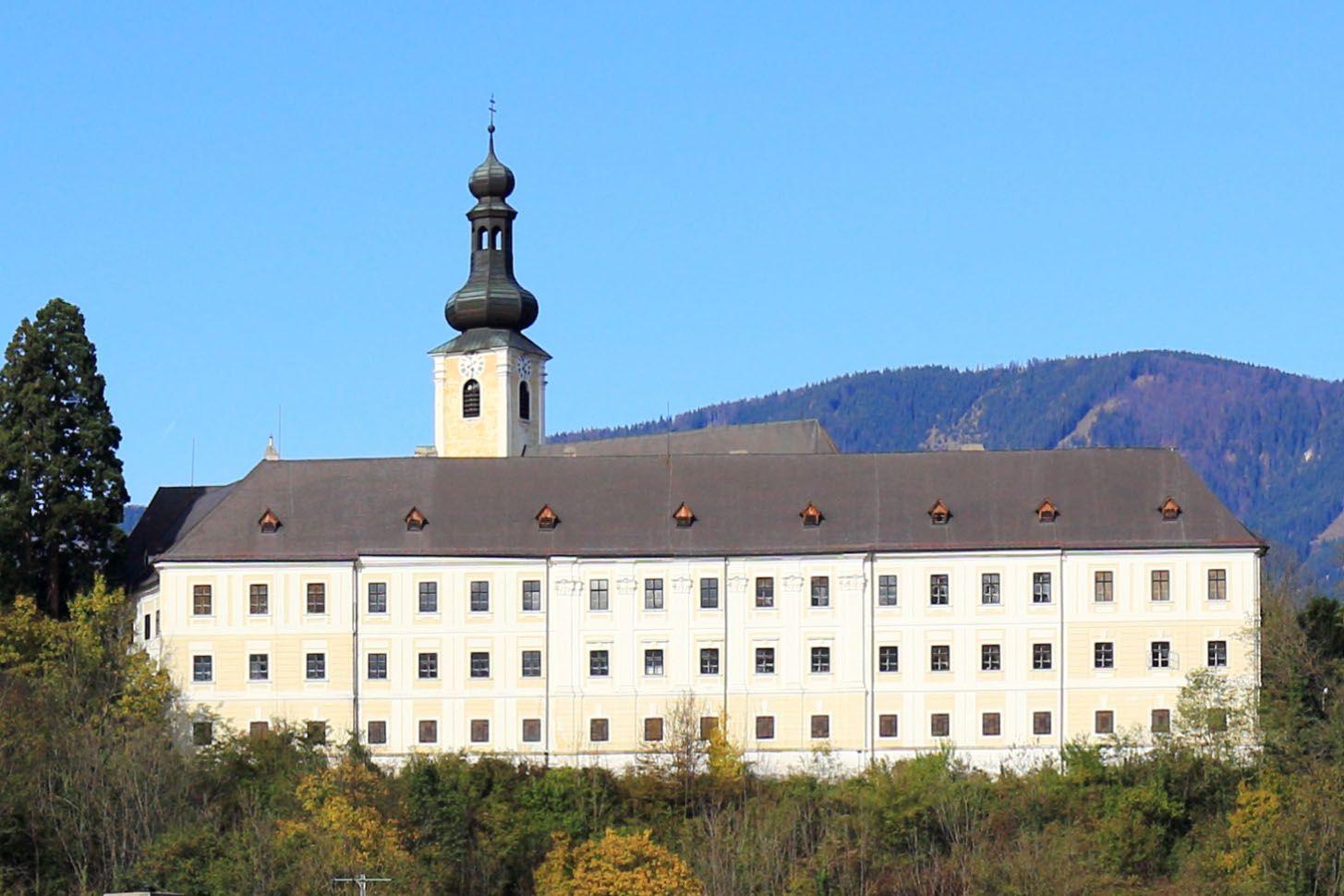 Hrad Gloggnitz pred zalesnenými kopcami a modrou oblohou.