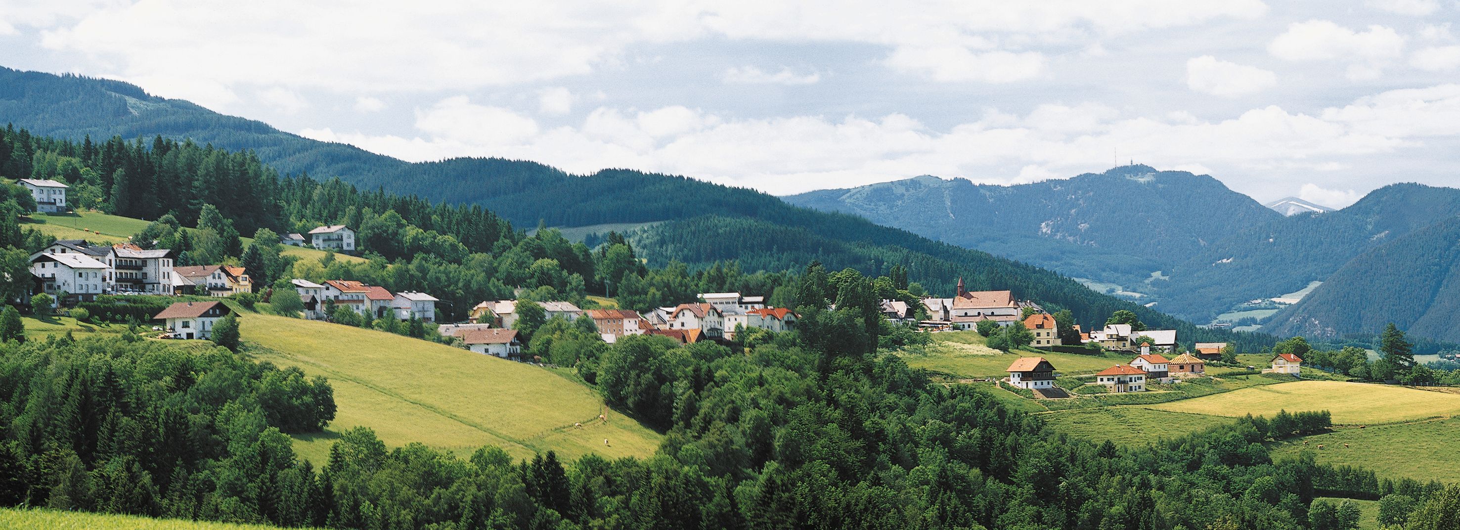 Panoráma mesta St. Corona am Wechsel so zelenými kopcami a horami v pozadí.