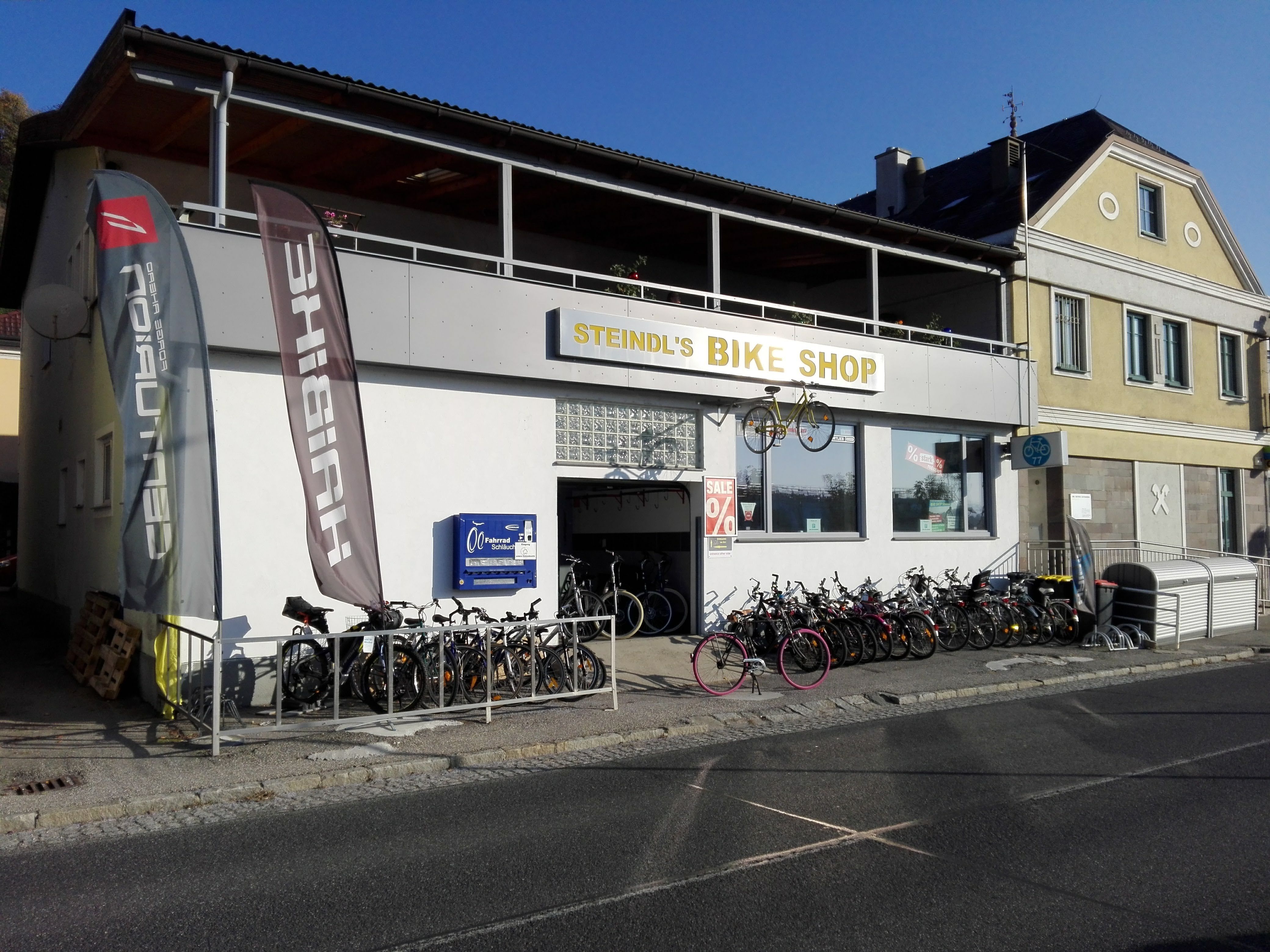 Obchod s bicyklami s bicyklami pred budovou a reklamnými vlajkami.