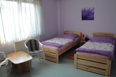 Jednoducho zariadená izba s dvoma samostatnými posteľami, malým stolom a dvoma stoličkami.