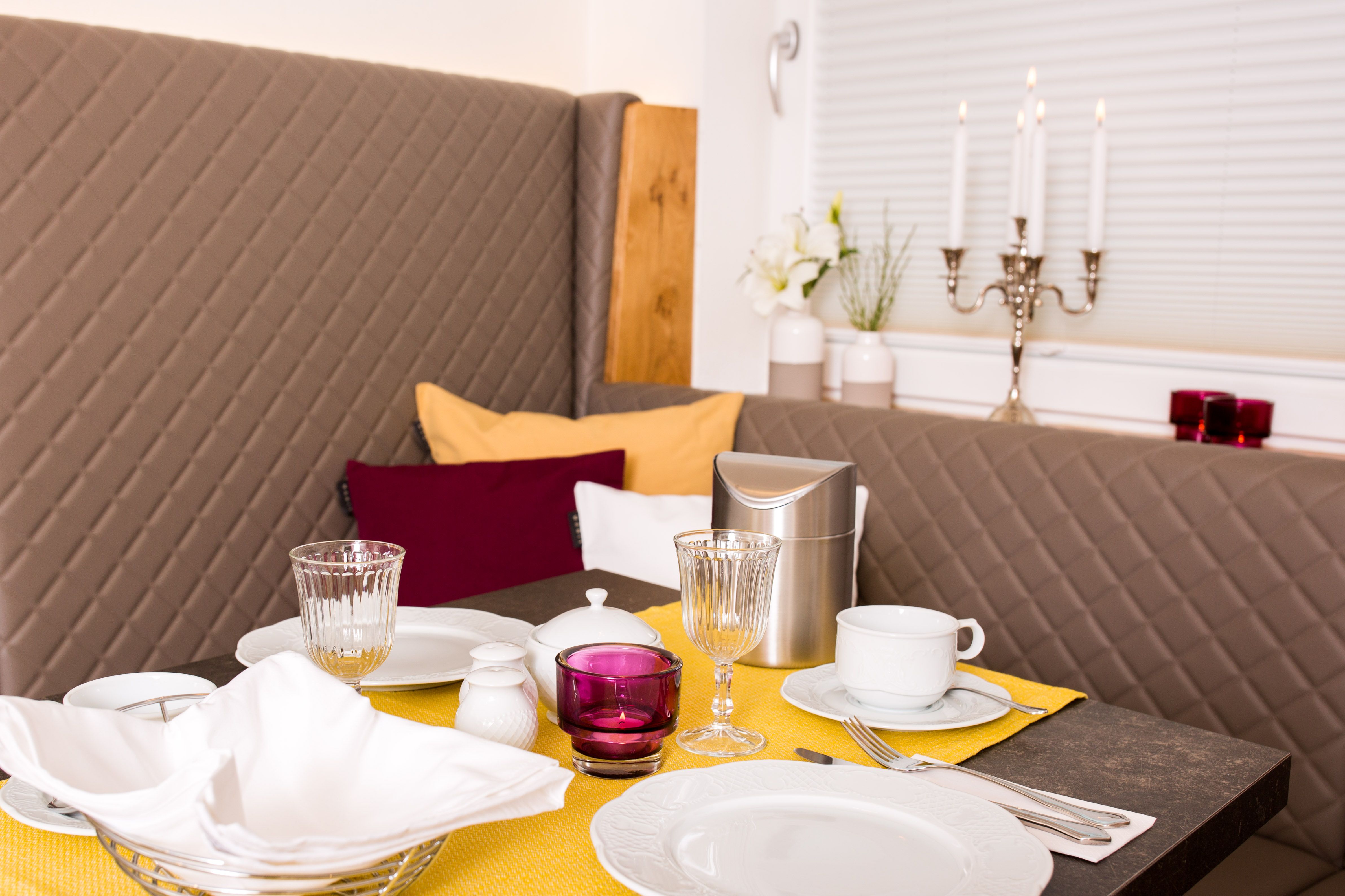 Elegantný raňajkový stôl so žltým behúňom, riadom, pohármi a svietnikmi.