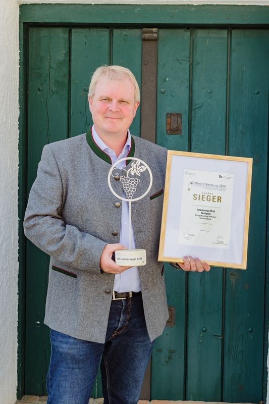 Osoba držiaca ocenenia a certifikát pred zelenými drevenými dverami.