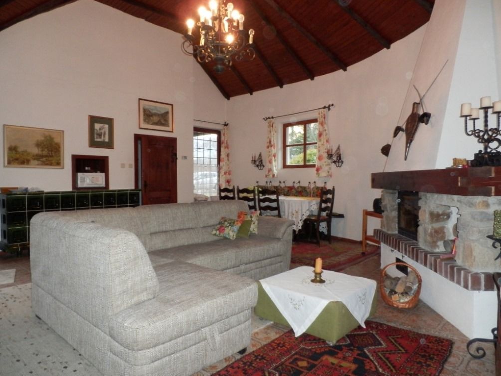 Útulná obývacia izba so sivou pohovkou, krbom a jedálenským stolom. Rustikálna výzdoba a drevený trámový strop.
