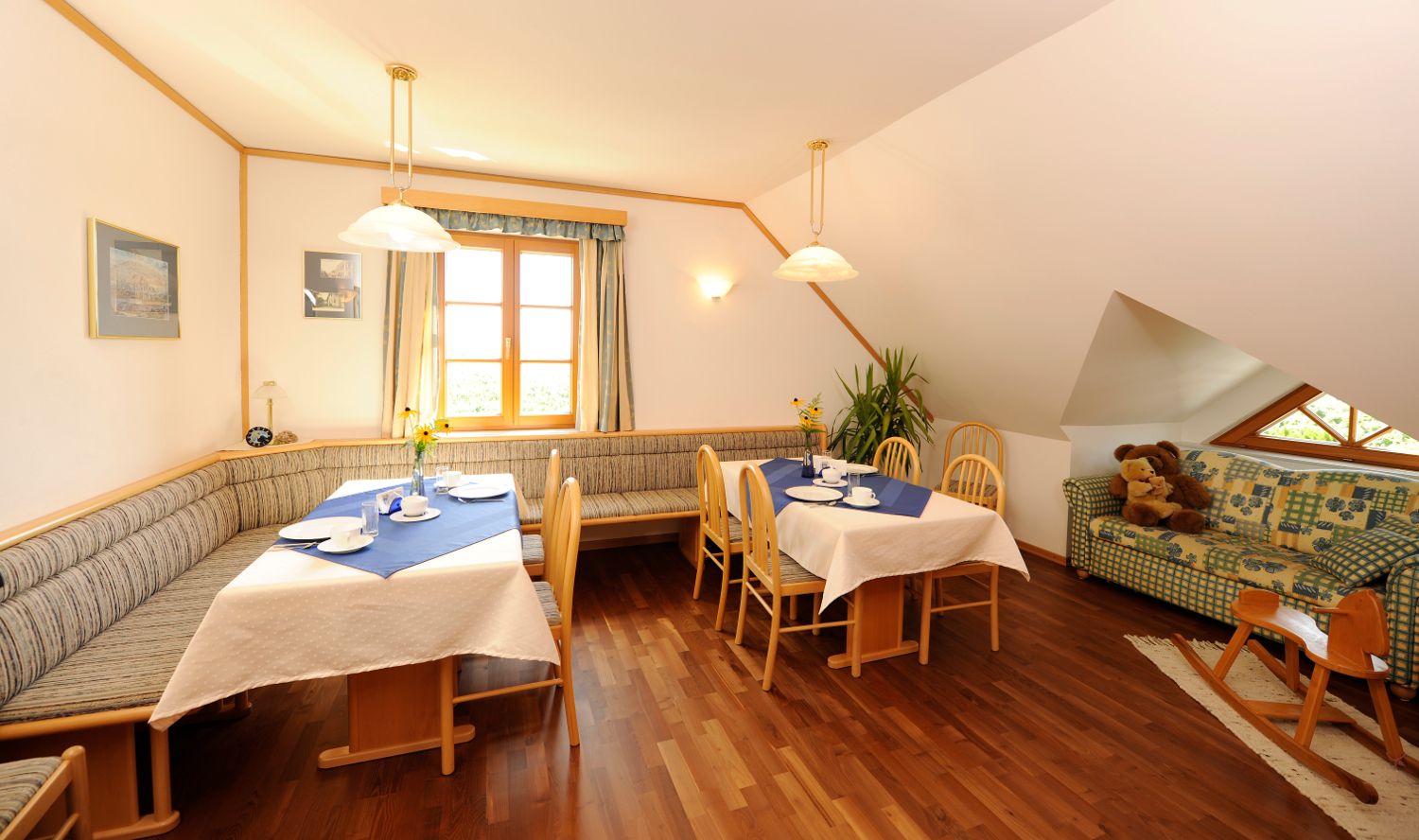 Útulná raňajková zóna s dreveným nábytkom, prestretými stolmi a pohovkou s plyšovými medvedíkmi.