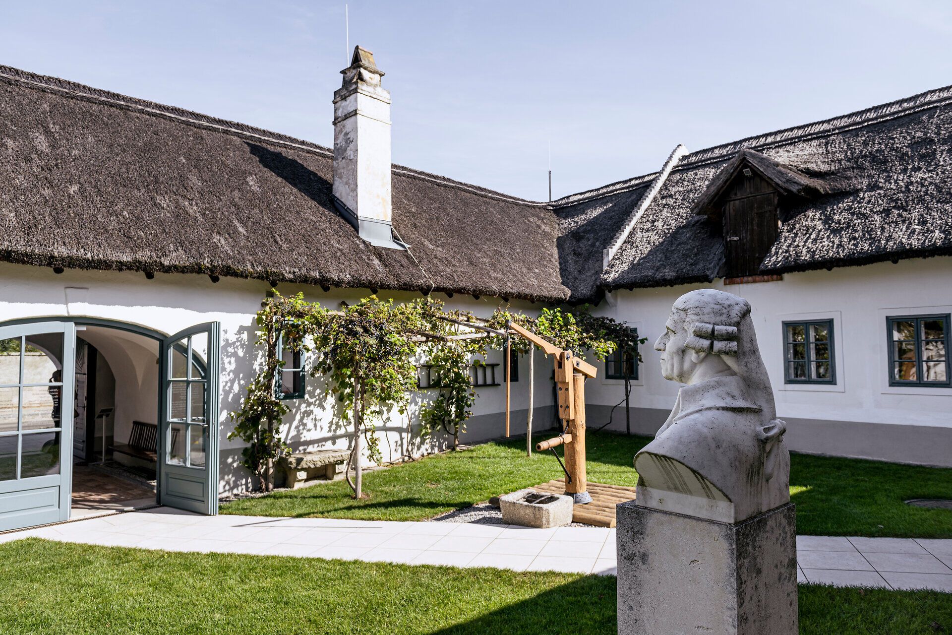 Vnútorné nádvorie Haydnovho rodného domu so slamenými strechami a Haydnovou bustou.