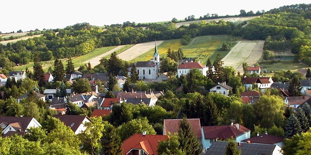Panoráma Unterolberndorfu s kostolom a okolitými domami pred zelenými kopcami.