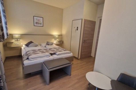 Hotelová izba s manželskou posteľou, drevenou podlahou a moderným nábytkom.