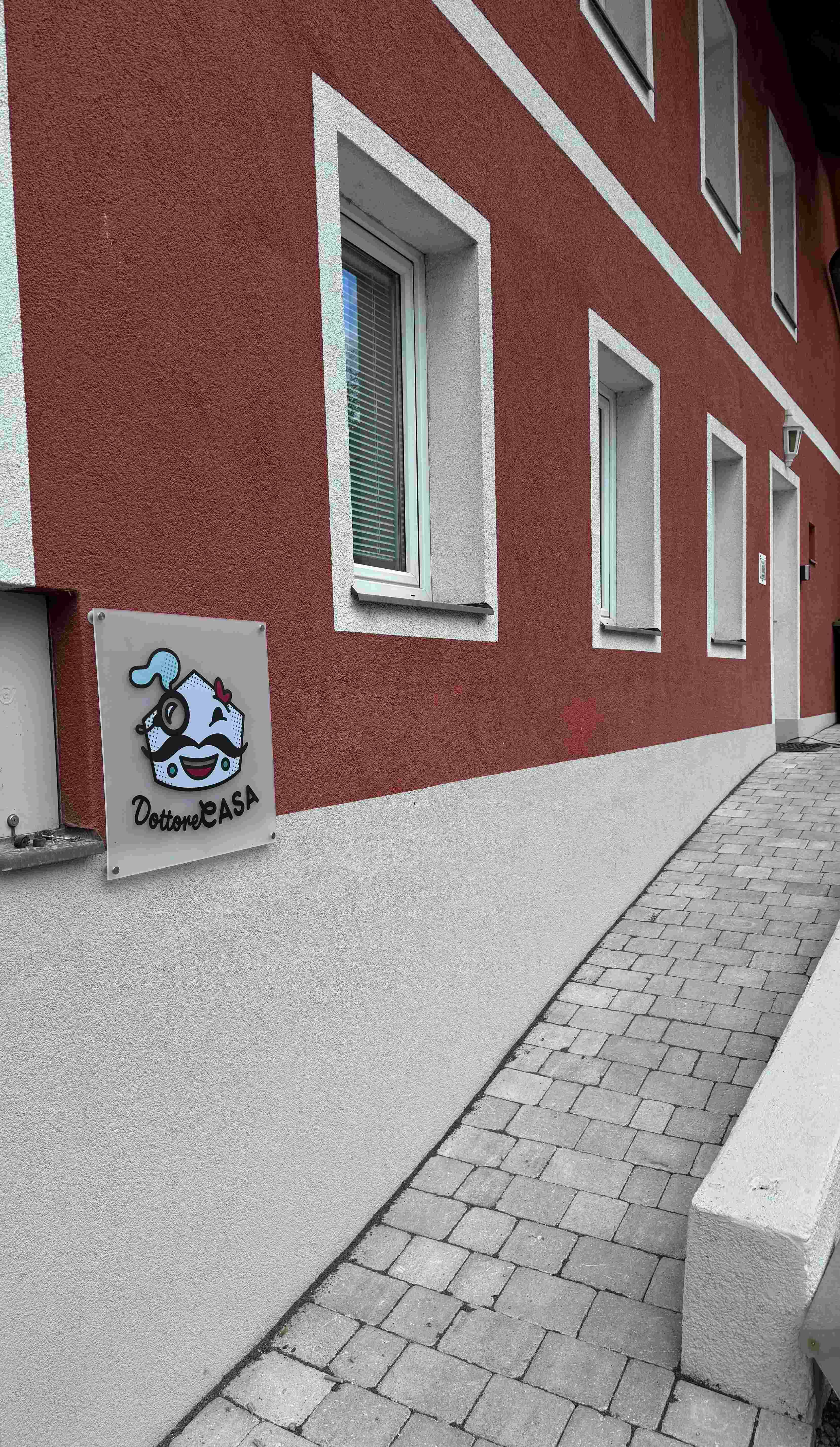 Pohľad zvonka na budovu s červenou fasádou a nápisom "Dottore Casa".