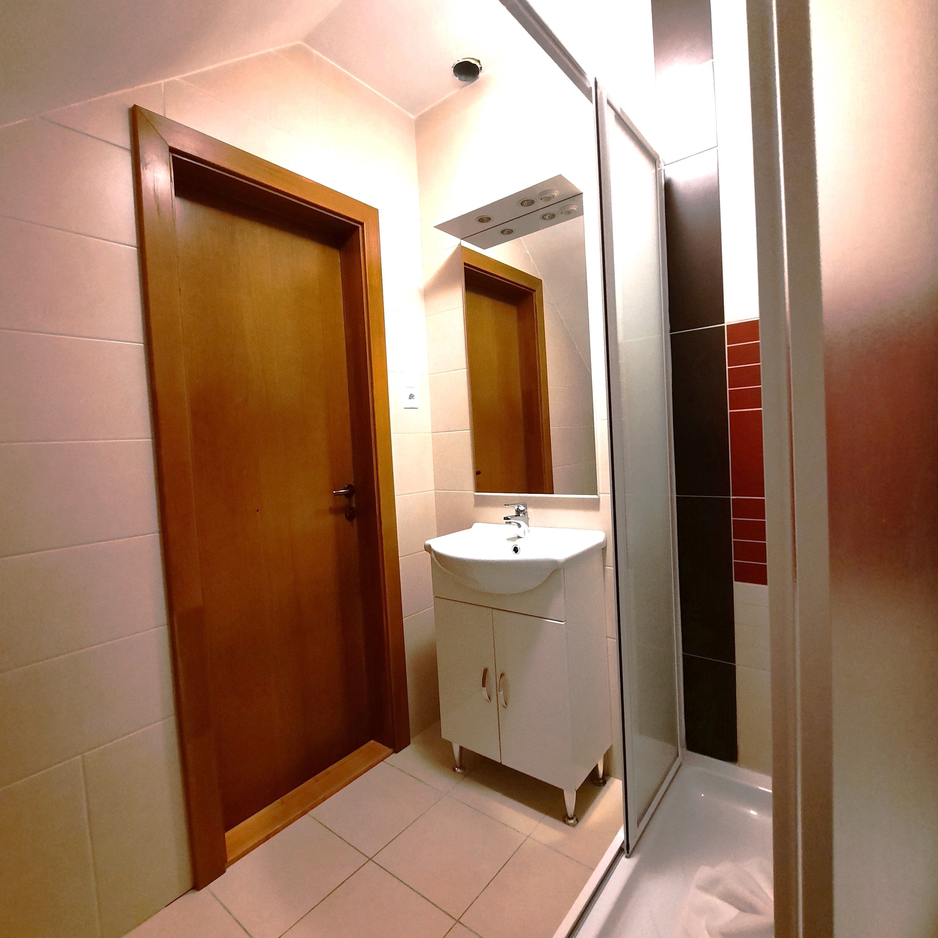 Moderná kúpeľňa s drevenými dverami, umývadlom a sprchovacím kútom.