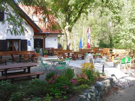 Vonkajší priestor chaty Schindlhütte so stolmi a stoličkami v zeleni.