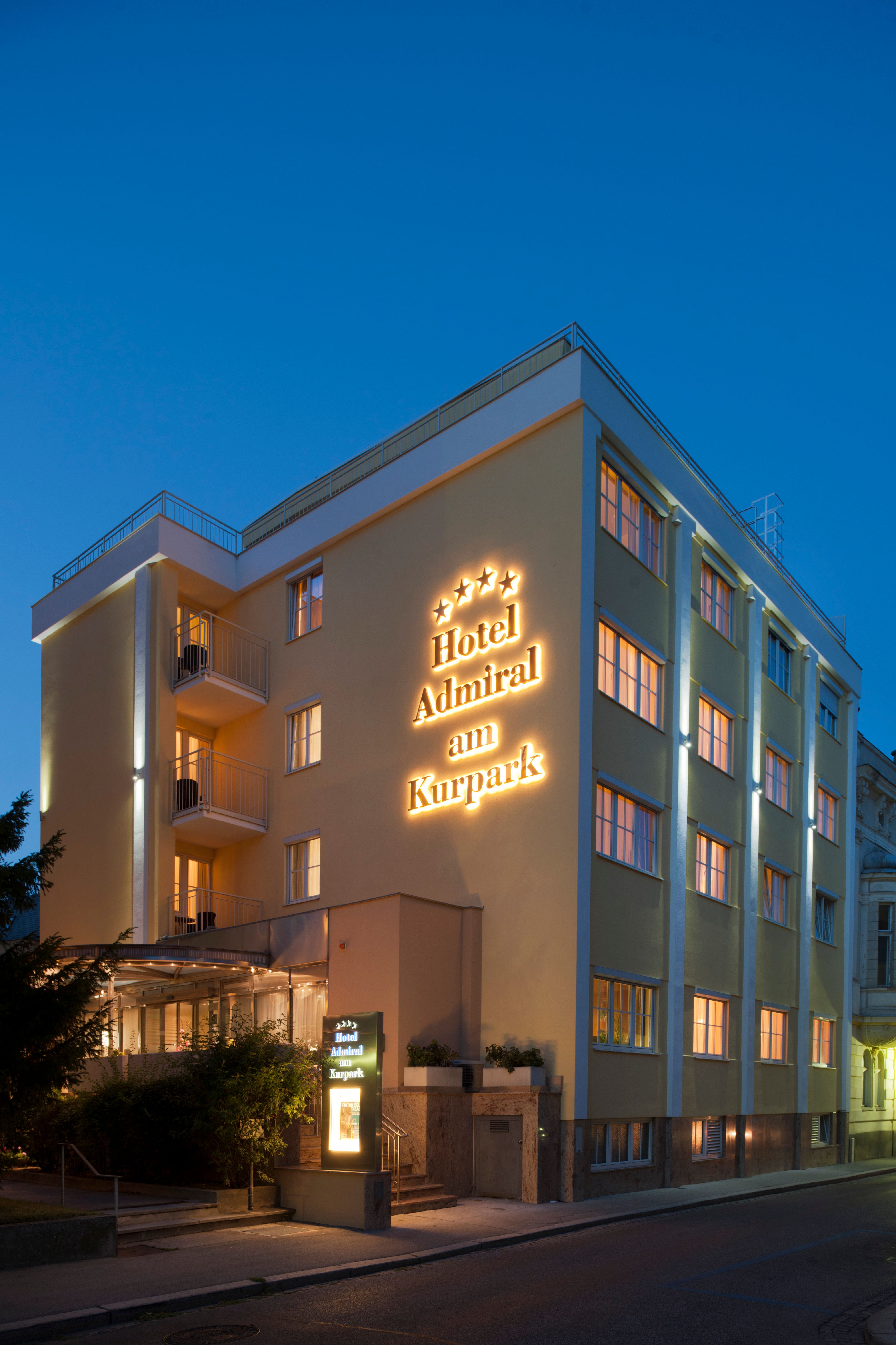 Exteriérový pohľad na hotel za súmraku s osvetleným nápisom "Hotel Admiral am Kurpark".